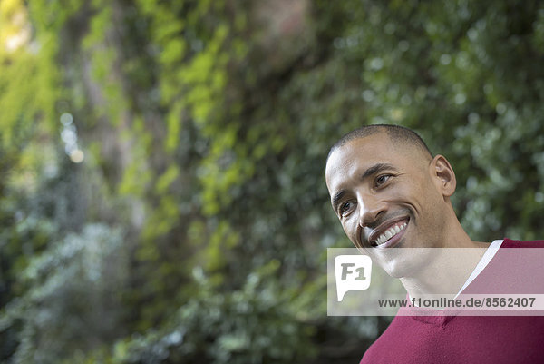 Scenes from urban life in New York City. A man smiling  in a relaxed mood  in a leafy space.