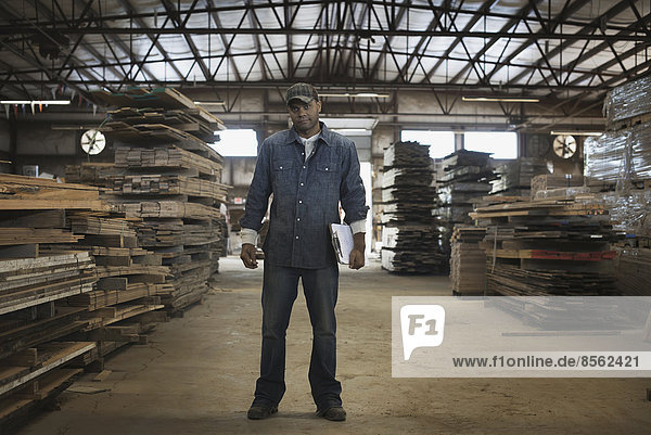 Ein Haufen recycelter Bohlen aus wiederverwertetem Altholz. Umweltgerechte Rückgewinnung in einem Holzlager. Ein Mann in einem Arbeitsoverall mit einem Klemmbrett.