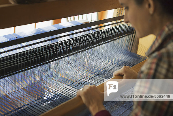 A woman seated at a wooden handloom creating a handwoven woollen fabric  with a blue and white pattern.