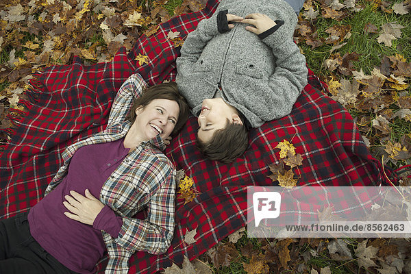Zwei Personen  eine Frau und ein Kind  liegen auf einer roten Schottenkaro-Picknickdecke und schauen nach oben.