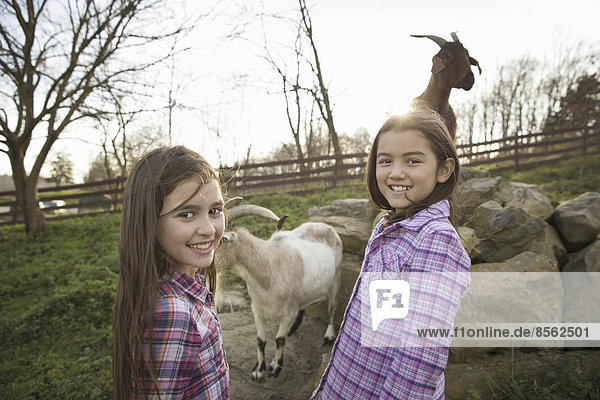 Two children  young girls  in the goat enclosure at an animal sanctuary.