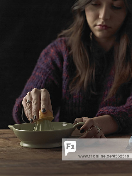 Eine Frau hält eine abgeschnittene Orangenhälfte und benutzt eine Orangenpresse  um den Saft zu extrahieren  auf einem Holztisch.