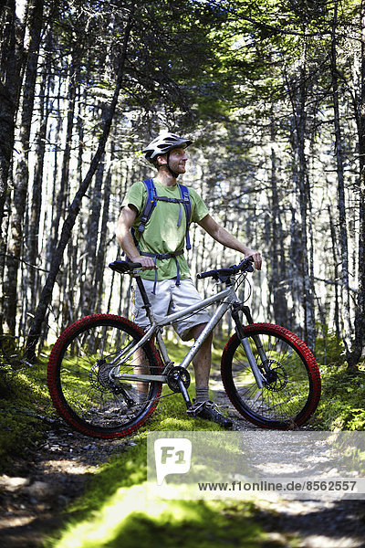 A mountain biker in a helmet with a rucksack standing by his bicycle in woodland.