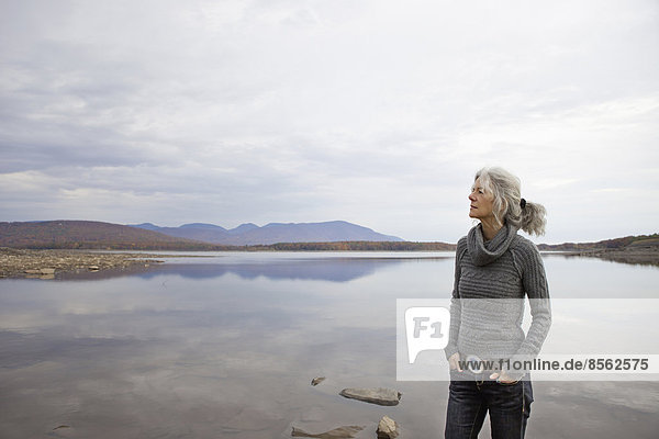 A woman looking out over the water on the shores of a calm lake.