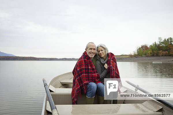 A couple  man and woman sitting in a rowing boat on the water on an autumn day. Sharing a picnic rug to keep warm.