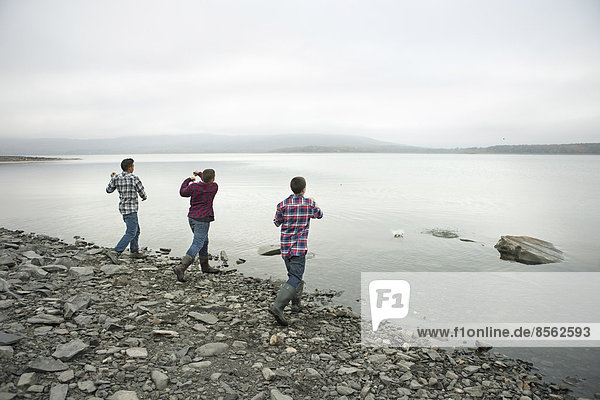 A day out at Ashokan lake. Three boys on the shore throwing skimmers pebbles across the water.