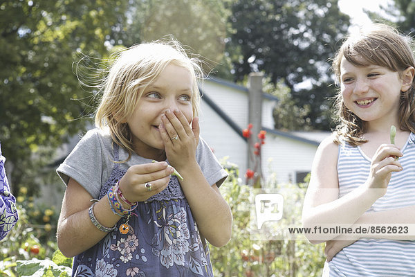 Zwei Kinder stehen draußen in einem Garten und lachen.