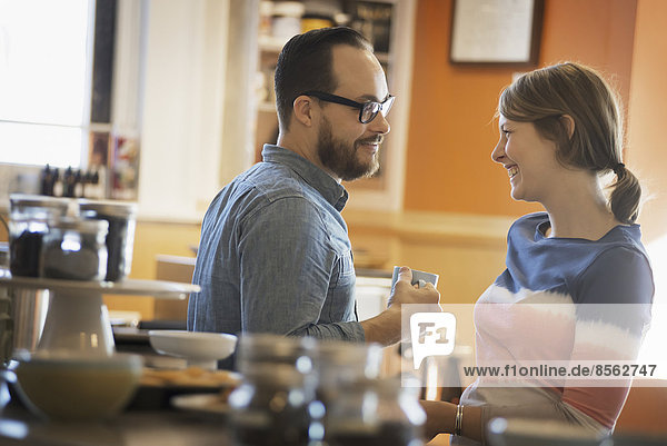 A couple sitting in a coffeeshop smiling and talking over a cup of coffee.