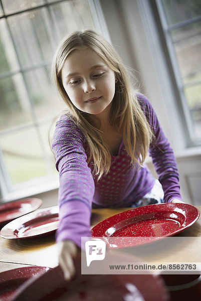 Ein Familienhaus. Ein junges Mädchen deckt den Tisch mit Tellern und Schüsseln für eine Mahlzeit.