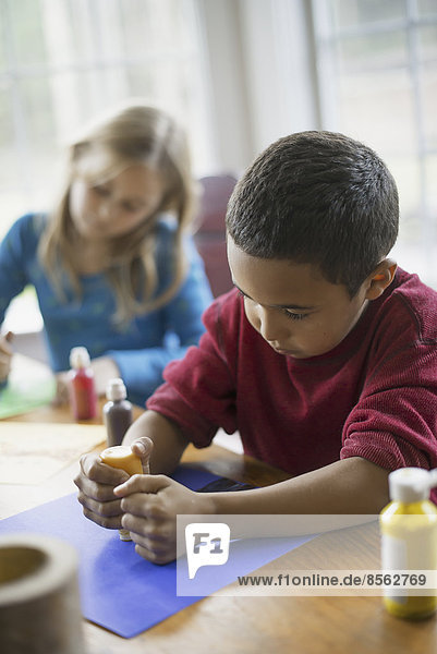 Kinder in einem Familienhaus. Zwei Kinder sitzen am Tisch und gestalten mit Farbe und Papier Dekorationen.