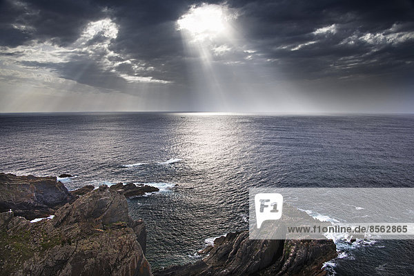 Die Küstenlinie von Cabo Sardao in Portugal. Sonne strömt durch Wolken auf das Meer.