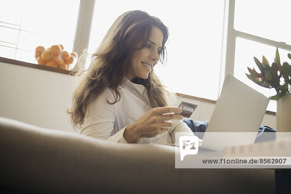 Woman on-line shopping on laptop on sofa with credit card