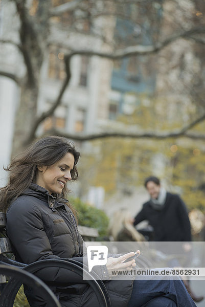 Woman seated in urban park with smartphone