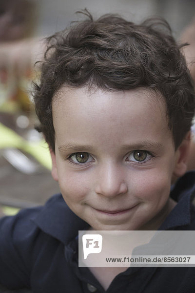 Ein kleiner Junge mit dunklem Haar und braunen Augen  der nach oben schaut und lächelt.