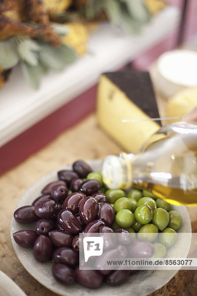 Ein Gericht aus frischem Bio-Gemüse. Grüne und schwarze Oliven auf einem Teller mit einem Spritzer Olivenöl aus einer Flasche. Fertiggerichte vom Bauernhof für eine Party