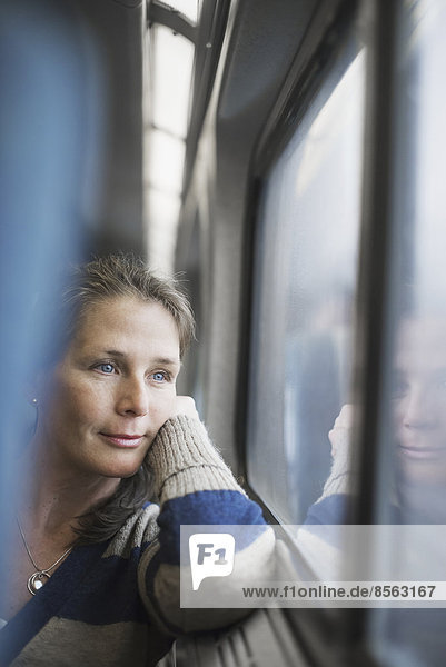 Eine Frau sitzt an einem Fensterplatz in einem Zugwaggon  den Kopf auf die Hand gestützt. Sie schaut in die Ferne.