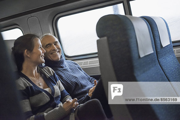Zwei Menschen sitzen lächelnd in einem Eisenbahnwagen. Sie machen eine Zugfahrt.