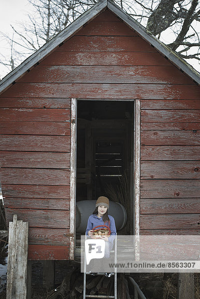 An organic farm in upstate New York  in winter. A girl sitting on the ladder of a henhouse with a basket of eggs.