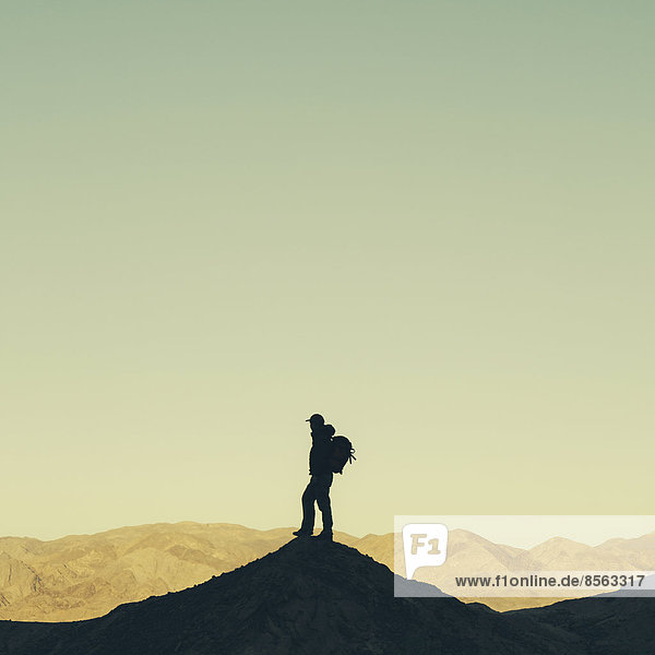 Silhouette eines männlichen Wanderers  der einen Rucksack trägt und auf einem Hügel im Death Valley Nationalpark steht.