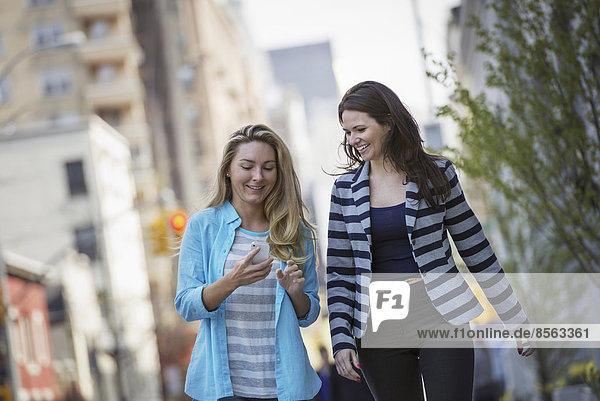 Menschen im Frühling in New York City im Freien. Zwei Frauen gehen zu Fuß  eine überprüft ihr Handy.