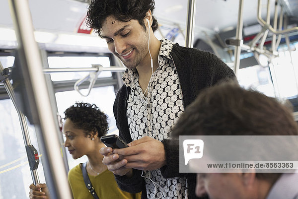 New Yorker Stadtpark. Menschen  Männer und Frauen in einem Stadtbus. Öffentliche Verkehrsmittel. In Kontakt bleiben. Ein junger Mann  der sein Mobiltelefon überprüft.