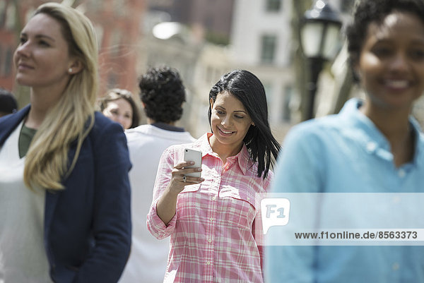 Menschen im Frühling in der Stadt im Freien. Der New Yorker Stadtpark. Drei Frauen  eine überprüft ihr Mobiltelefon.