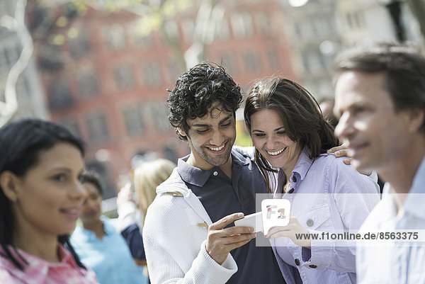 Menschen im Frühling in der Stadt im Freien. New York City. Eine Gruppe von Männern und Frauen  ein Paar im Zentrum  das auf ein Handy schaut.