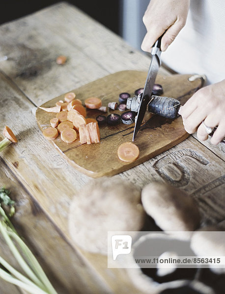 Eine häusliche Küchentischplatte. Eine Person  die frisches Gemüse auf einem Schneidebrett mit einem Messer schneidet.