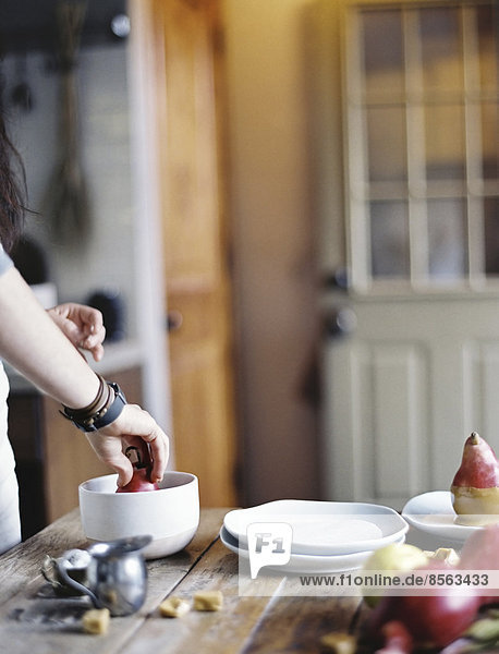 Eine Frau in einer Haushaltsküche beim Kochen. Sie taucht frische Bio-Birnen in eine Sauce zum Dessert. Frische Zutaten. Braune Zuckerwürfel