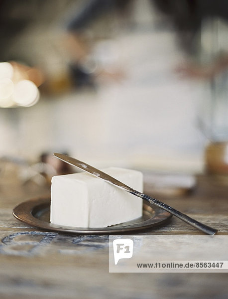 Eine häusliche Küche. Eine Frau im Hintergrund. Eine Platte frischer Bio-Butter auf einer Holzschale.