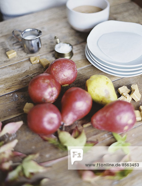 Eine häusliche Küchentischplatte. Eine kleine Gruppe frischer Bio-Birnen und ein Stapel weißer Teller.