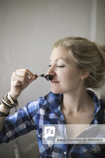 A young woman with blonde hair  holding a aromatic plant or herb flower to her nose and inhaling the aroma.