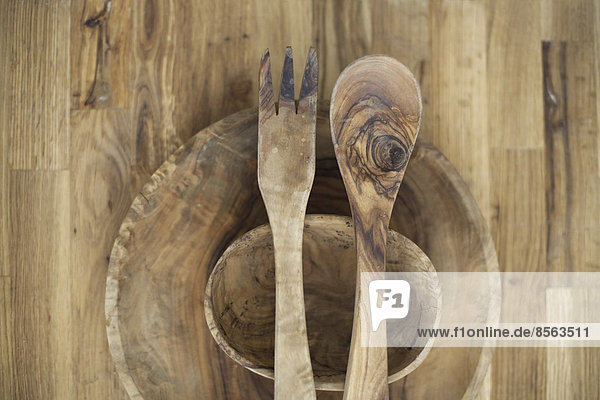 Eine hölzerne Tischplatte mit zwei kleinen gedrehten Schüsseln und zwei hölzernen Salatbestecken. Holzmaserung und natürliche Muster.