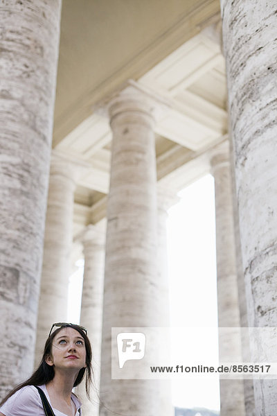 Eine Frau schaut zu den hohen Säulen und Bögen eines historischen Gebäudes in Rom auf.