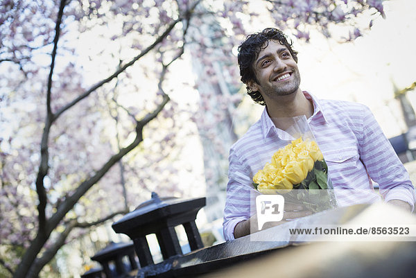 Stadtleben. Ein junger Mann im Frühling im Park mit einem Strauß gelber Rosen in der Hand.