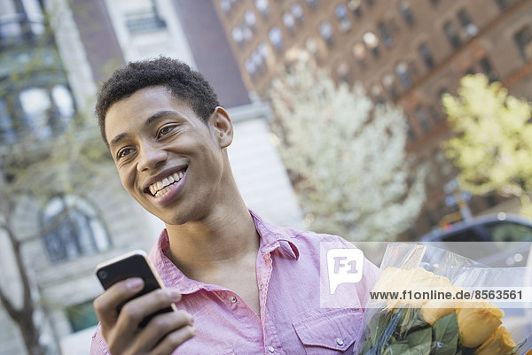 Urbaner Lebensstil. Ein junger Mann mit kurzen schwarzen Haaren  der ein rosa Freizeithemd trägt. Er hält ein Smartphone in der Hand.