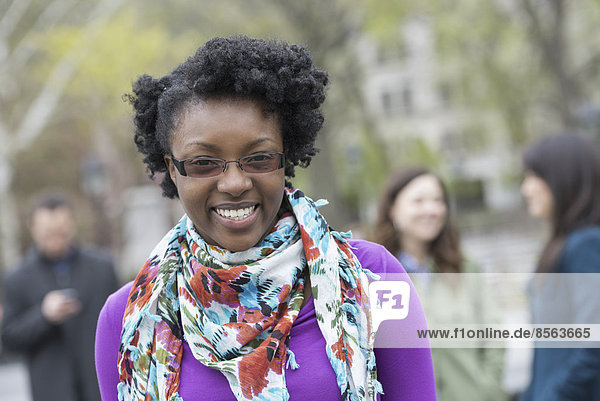 A group of people in a city park. A young woman smiling  wearing a purple shirt and floral scarf.