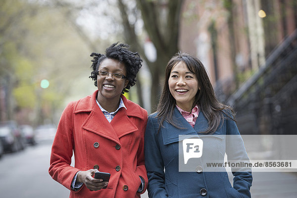 Zwei Frauen Seite an Seite auf einer Straße in der Stadt. Eine hält ein Mobiltelefon in der Hand.