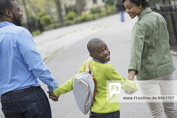 Ein New Yorker Stadtpark im Frühling. Ein Junge mit einer Büchertasche  der mit seiner Mutter und seinem Vater Händchen hält.