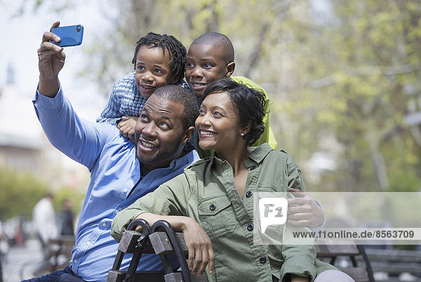 A New York city park in the spring. A family  parents and two boys taking a photograph with a smart phone.