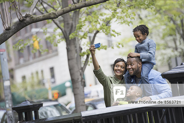Ein New Yorker Stadtpark im Frühling. Ein Junge  der auf den Schultern seines Vaters reitet  und eine Frau  die mit einem Smartphone ein Selbstfoto macht.
