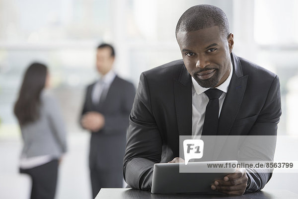 Junge Berufstätige bei der Arbeit. Ein Mann in einem Geschäftsanzug  der ein digitales Tablett benutzt.