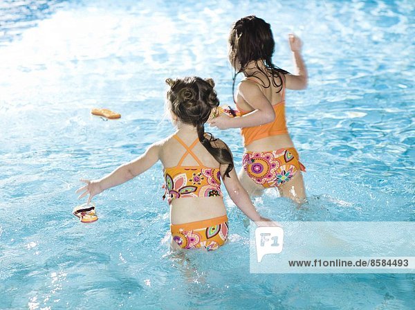 Two girl running in water at the swimming pool  seen from back