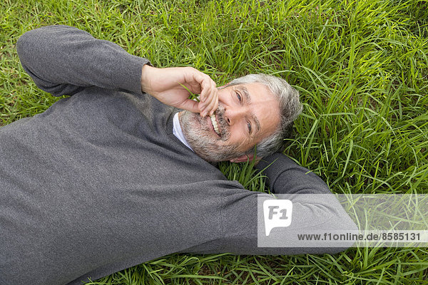 Reifer Mann lächelnd auf dem Gras liegend