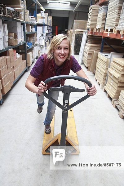 France  young woman using transpallet in warehouse.