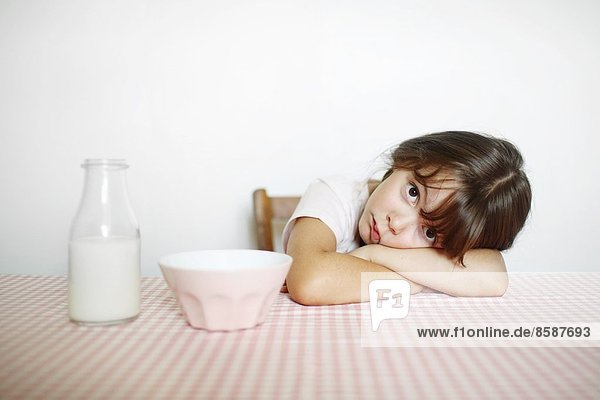 Ein kleines Mädchen sitzt an ihrem Frühstückstisch mit einer Schüssel Milch.