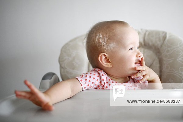 A baby girl eating a cake in her high chair