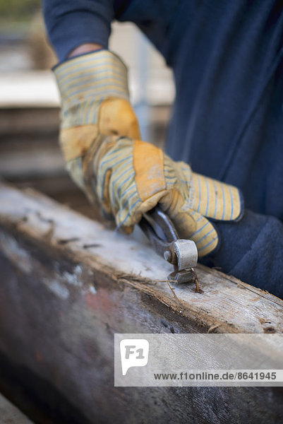 Eine zurückgewonnene Holzwerkstatt. Ein Mann bereitet das Holz vor  indem er alle Nägel und Bolzen entfernt.