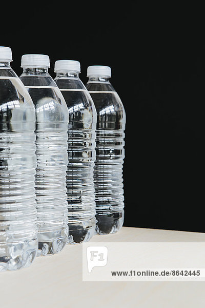 Reihe von klaren  mit gefiltertem Wasser gefüllten Plastik-Wasserflaschen in einer Reihe. auf schwarzem Hintergrund.