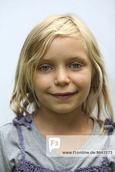 A young girl with blonde hair  and blue eyes. Smiling and looking at the camera.